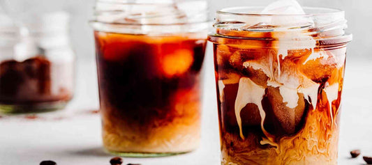 Iced mocha served in glass jars with coffee ice cubes, cocoa, and cream swirling together.