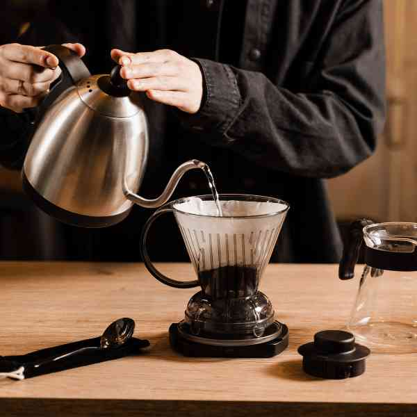 Person pouring water from a kettle into a coffee filter on a wooden table.