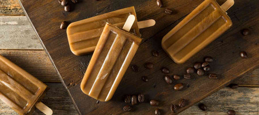 Frozen coffee popsicles made with Dancing Moon Coffee®, displayed on a rustic wooden board with scattered coffee beans