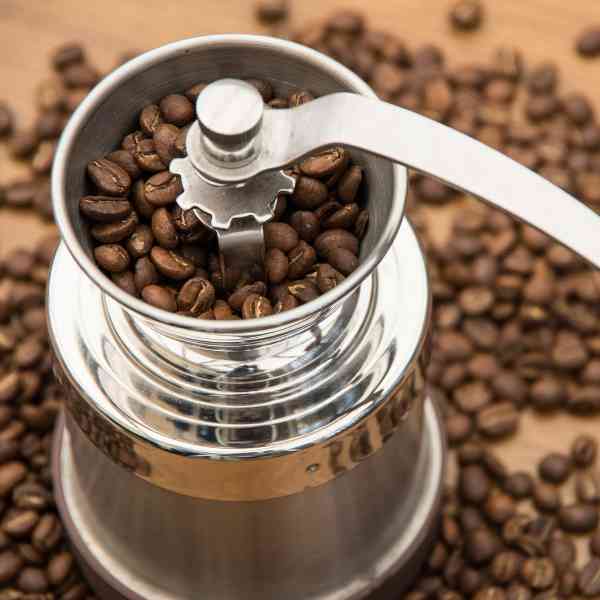 Hand grinder with coffee beans on a background of scattered coffee beans