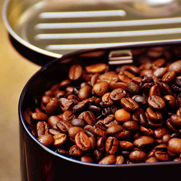 Open container of coffee beans with a metal scoop on a wooden surface