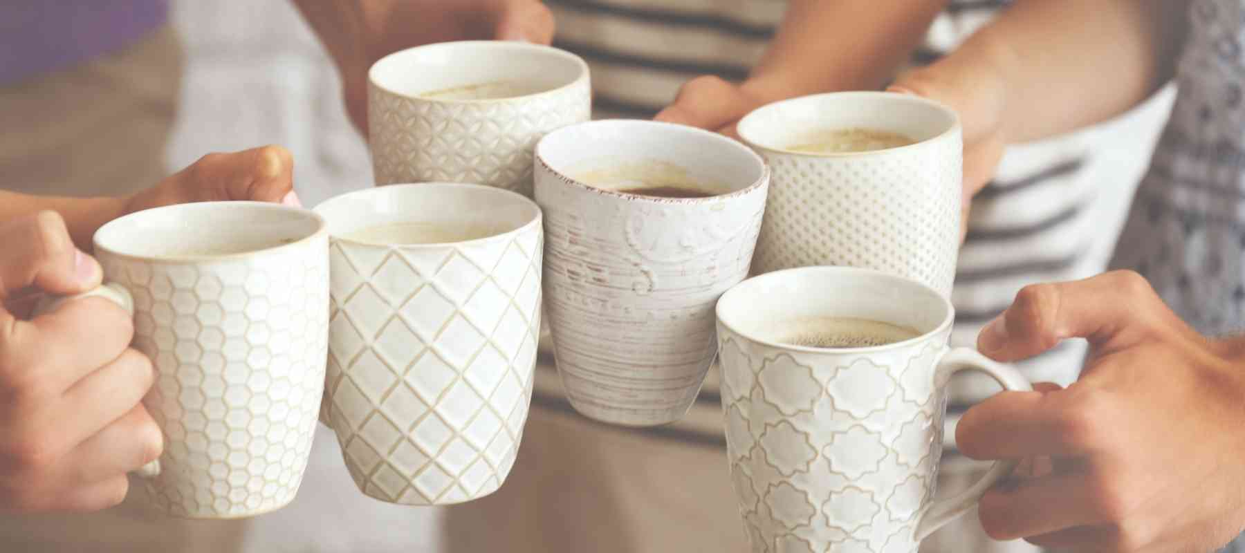 People holding white ceramic mugs with patterns on a blurred background